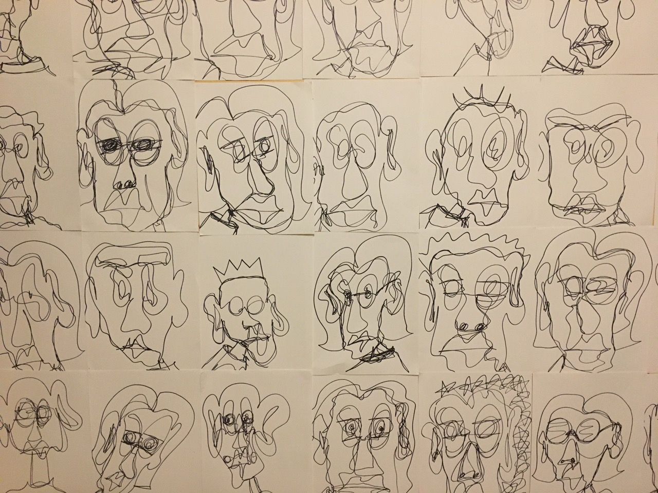 wall covered in grid of many pieces of paper with abstract portraits done in marker