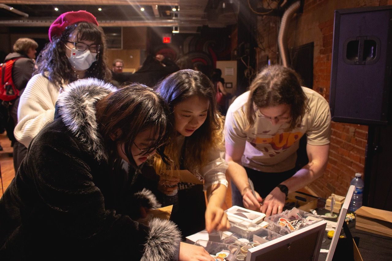 4 people leaning over a table of postcards and drawing supplies