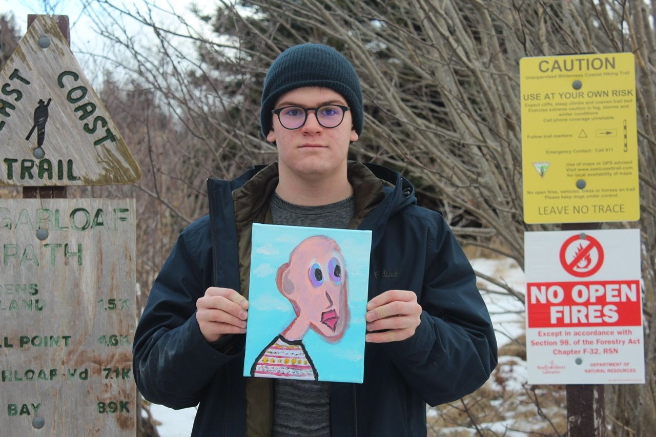 myself holding a small painting outside in winter with trail signs on either side