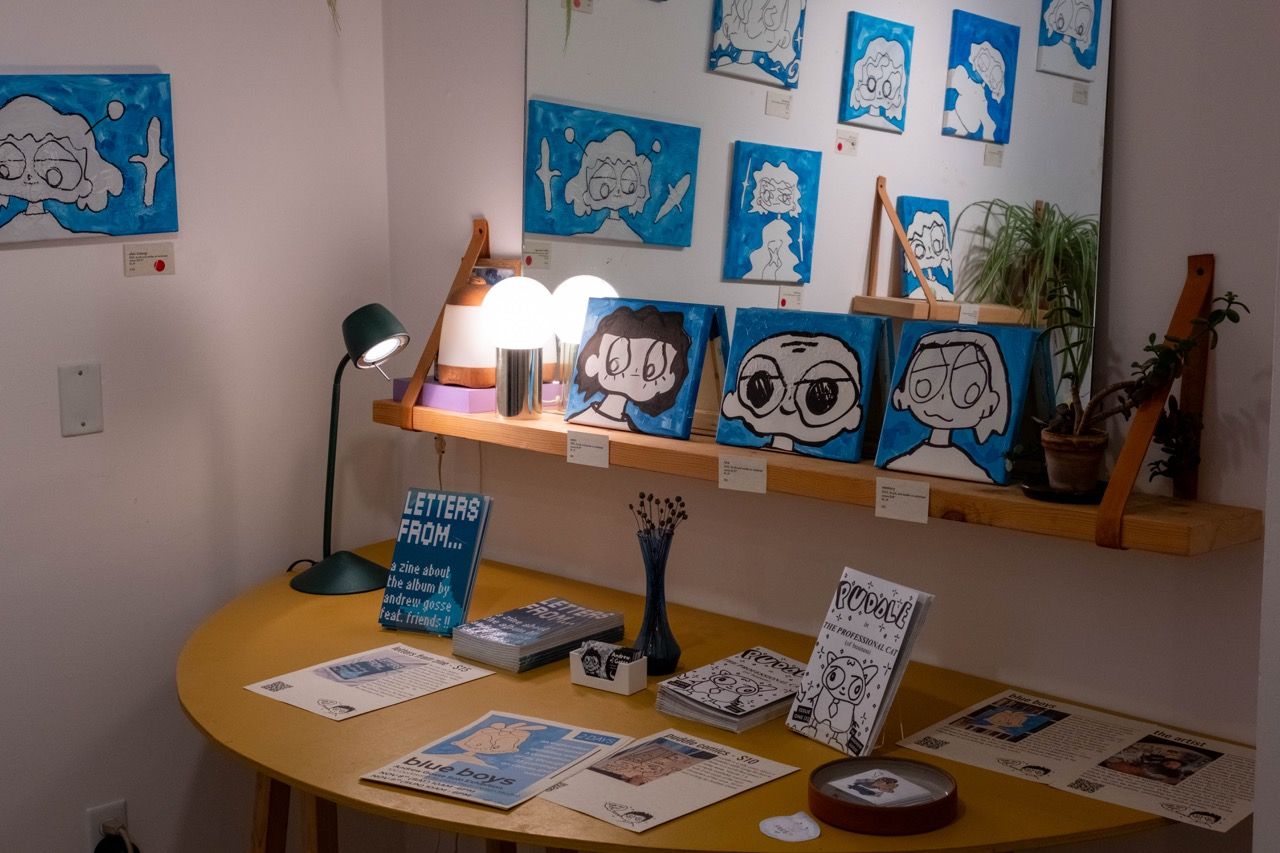 yellow table with various books on display, blue paintings in background and more visible in mirror off camera