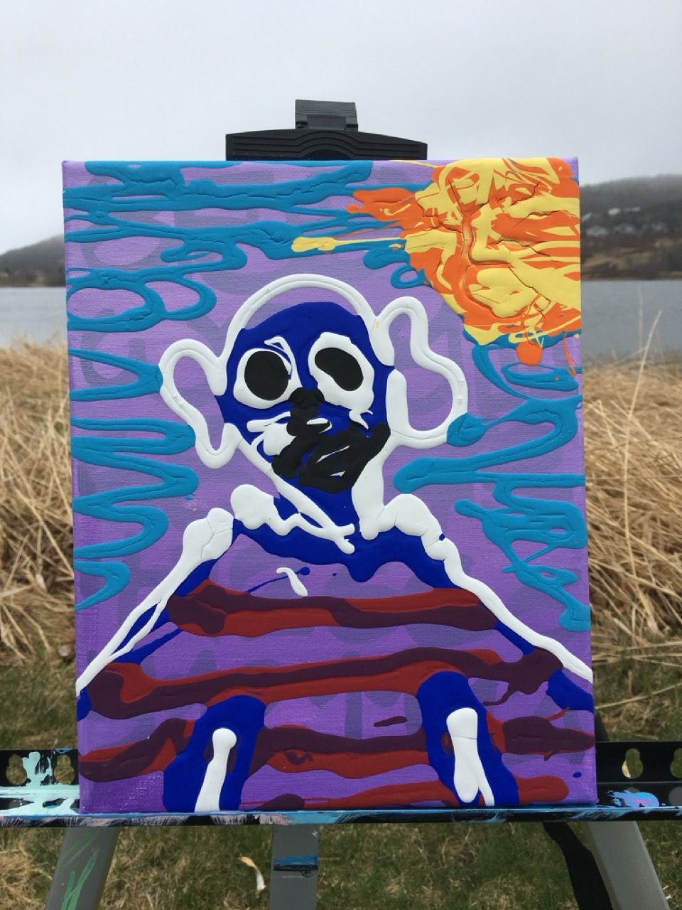 abstract figural painting on easel outside in front of body of water