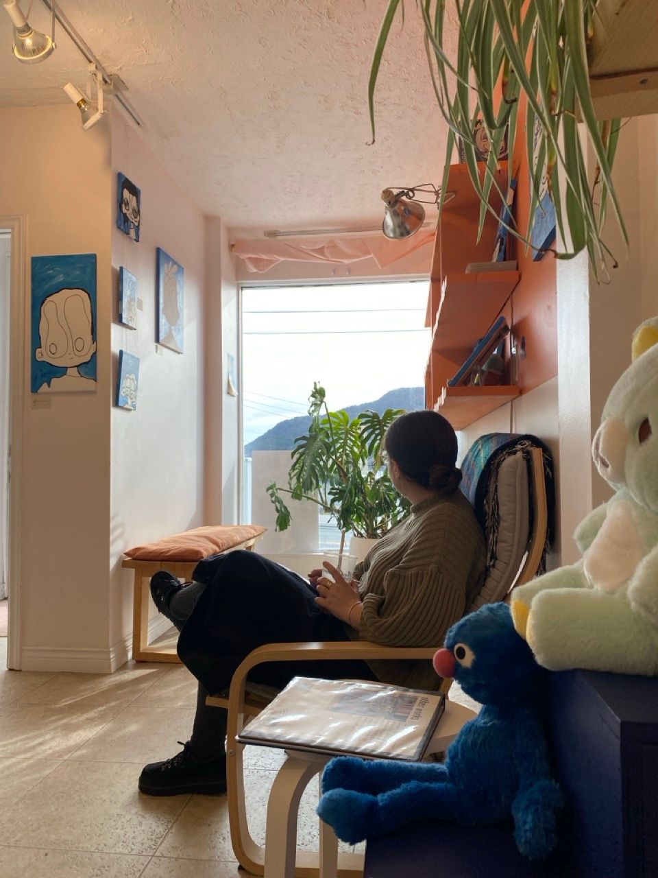 person sitting looking away from camera with large window and blue paintings on walls in background