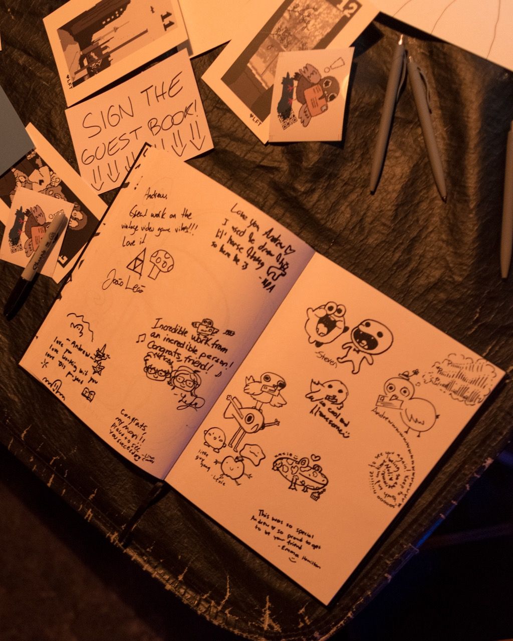 book laid out on table filled with drawings and messages from friends - "SIGN THE GUEST BOOK" written on paper next to book